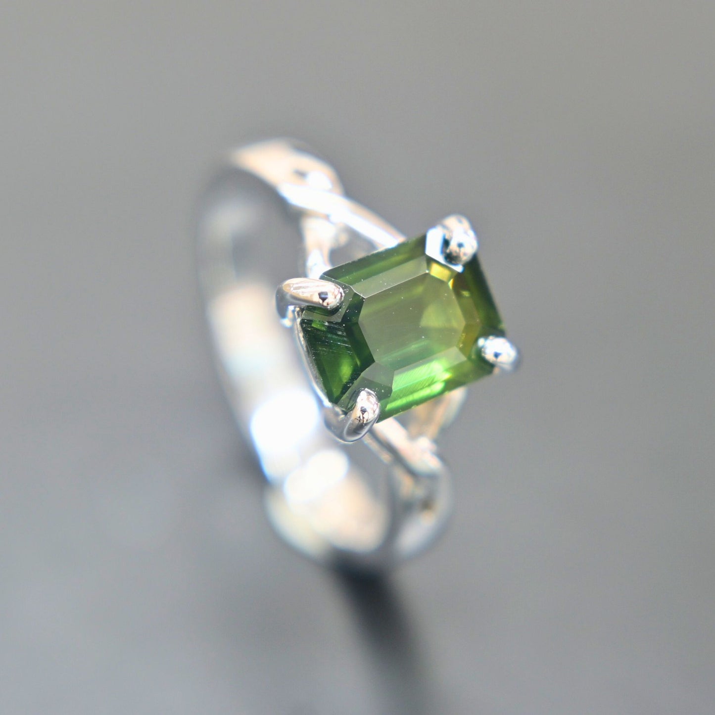 18K white gold ring featuring an emerald-cut green sapphire in a four-prong setting with a twisted band design.