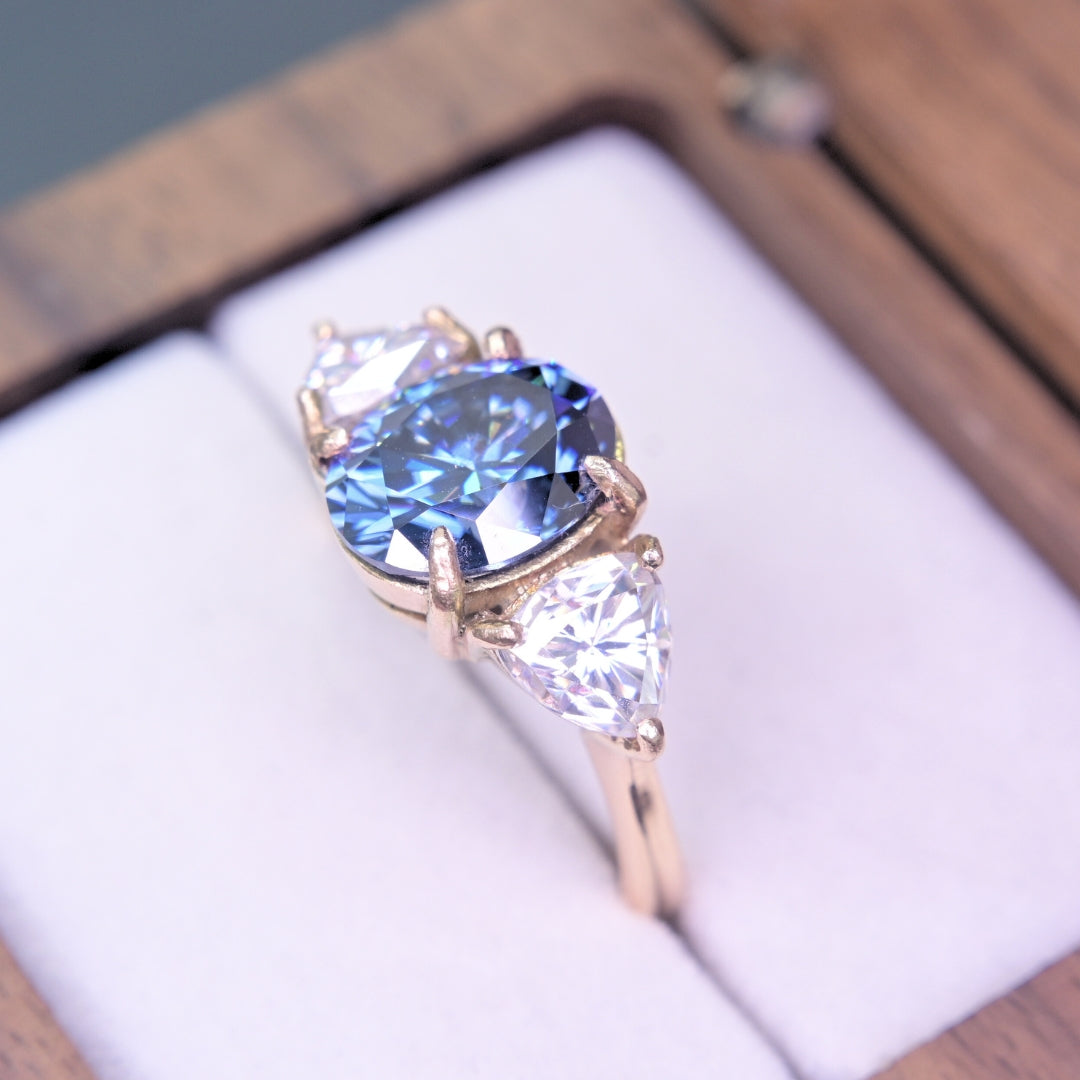 Ring with blue moissanite and gold setting on a white box