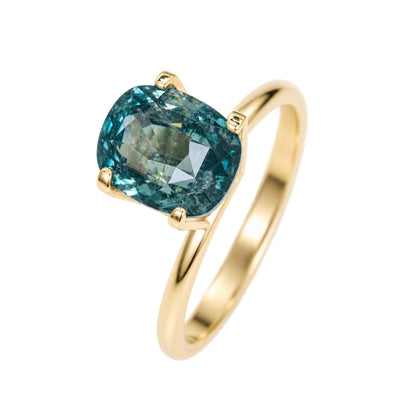 Unheated 2.13ct cushion teal sapphire placed over a ring setting frame for custom engagement ring design.